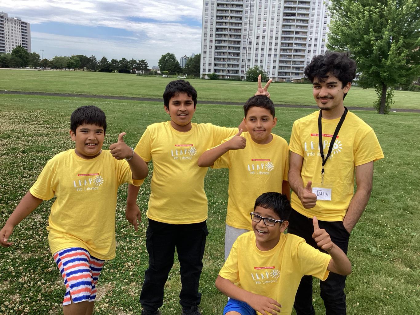 Photo of four LEAP into Literacy Summer Day Camp program participants and one volunteer standing in a park and smiling at the camera