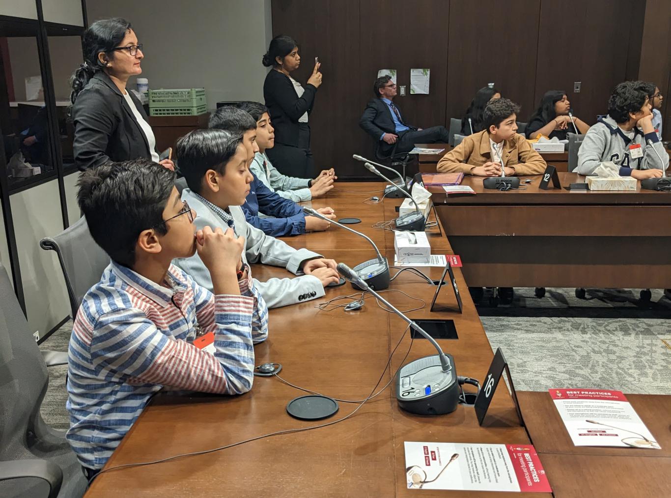Photo of Take the LEAD program participants sitting around a large debate table equipped with microphones