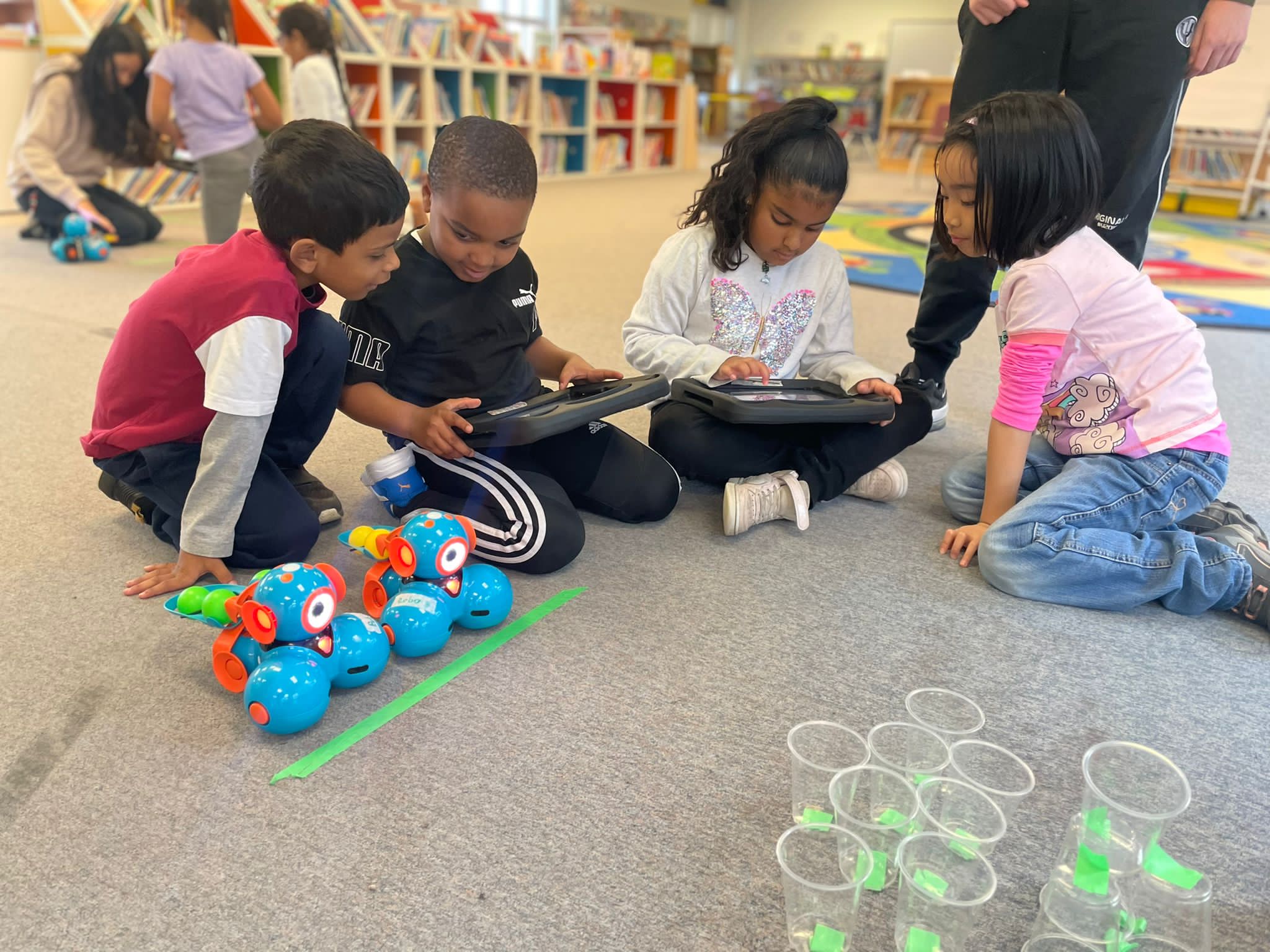 Photo of four LiftED program participants sitting on the floor of a classroom and looking at computer tablets
