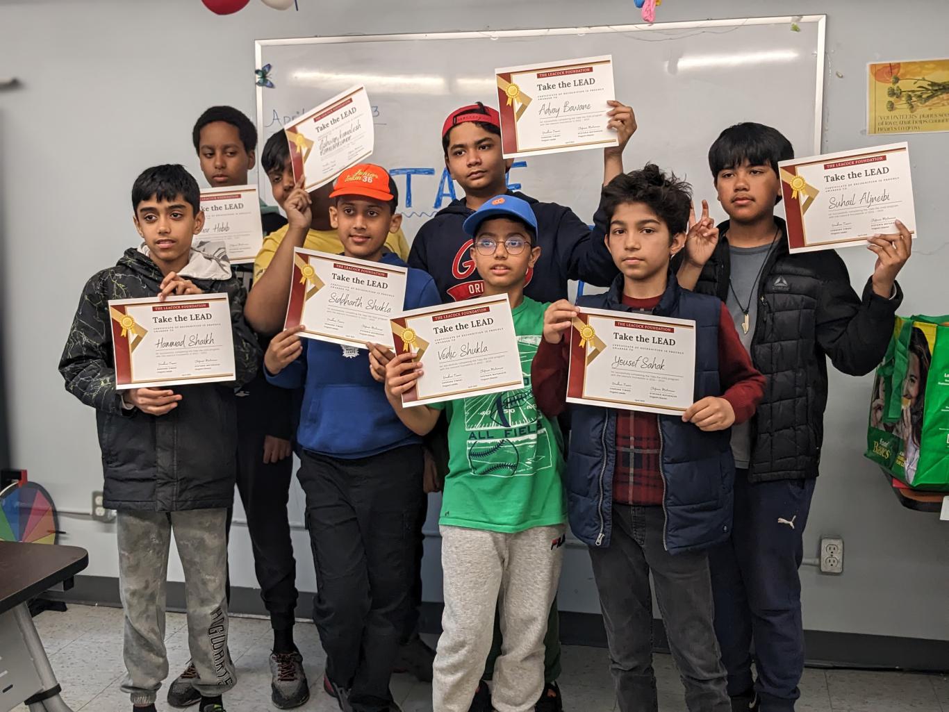 Photo of eight Take the LEAD program participants standing in a classroom and holding up program completion certificates